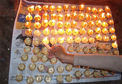 a photograph of a hand lighting many small votive candles set on newspapers on the ground in Nepal as part of a religious ceremony
